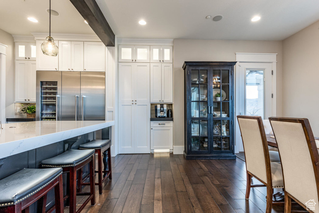 Kitchen with built in fridge, dark wood finished floors, white cabinetry, glass insert cabinets, and hanging light fixtures