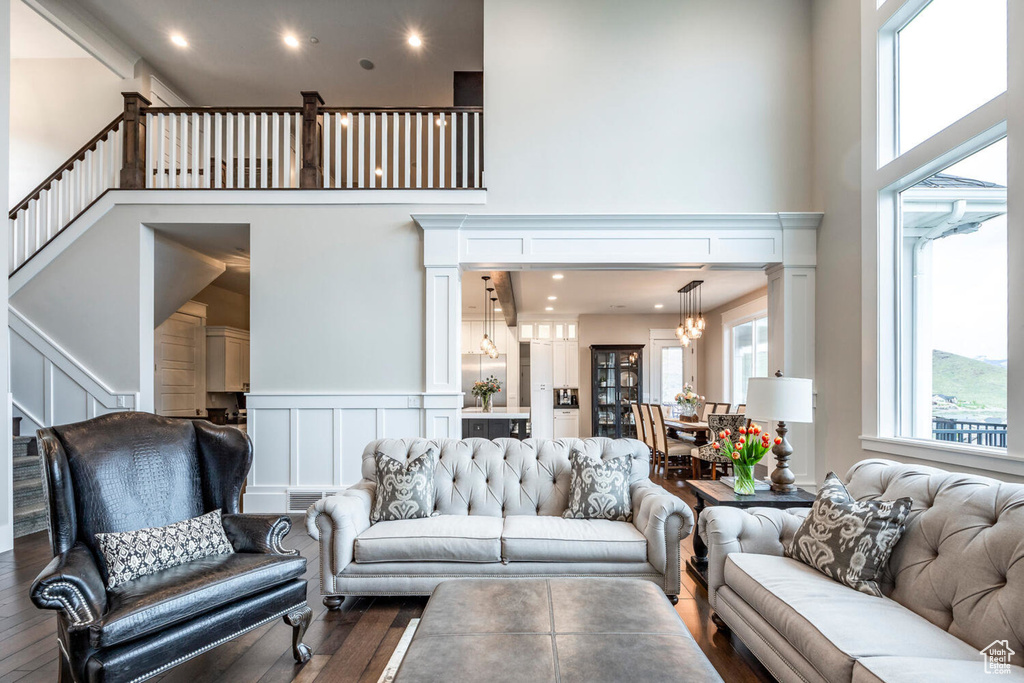 Living room with a high ceiling, healthy amount of natural light, wood finished floors, a decorative wall, and a chandelier