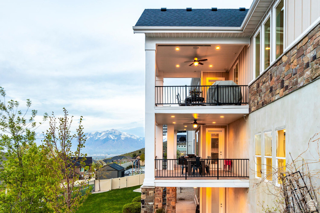 Rear view of house featuring a balcony, board and batten siding, a ceiling fan, a mountain view, and a shingled roof