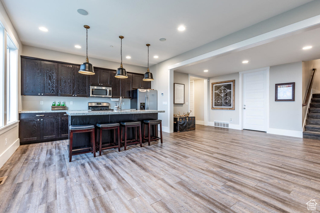 Kitchen with appliances with stainless steel finishes, light wood-style flooring, a breakfast bar area, recessed lighting, and a center island with sink
