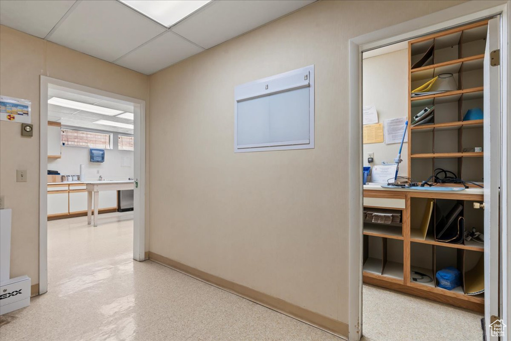 Corridor featuring a desk, baseboards, and a paneled ceiling