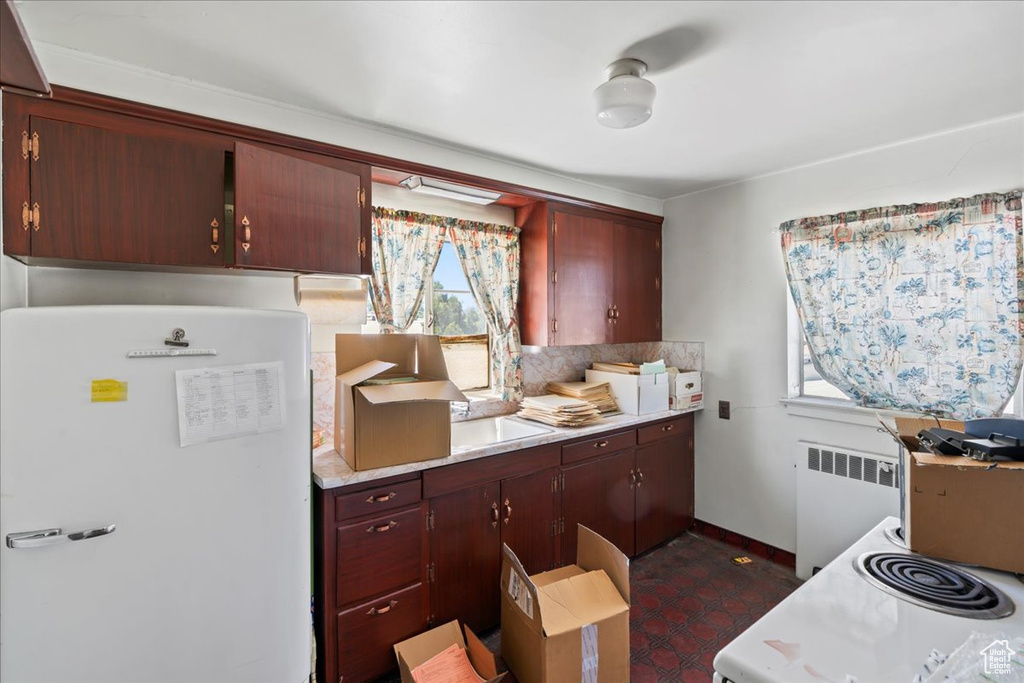 Kitchen with freestanding refrigerator, radiator heating unit, light countertops, decorative backsplash, and baseboards