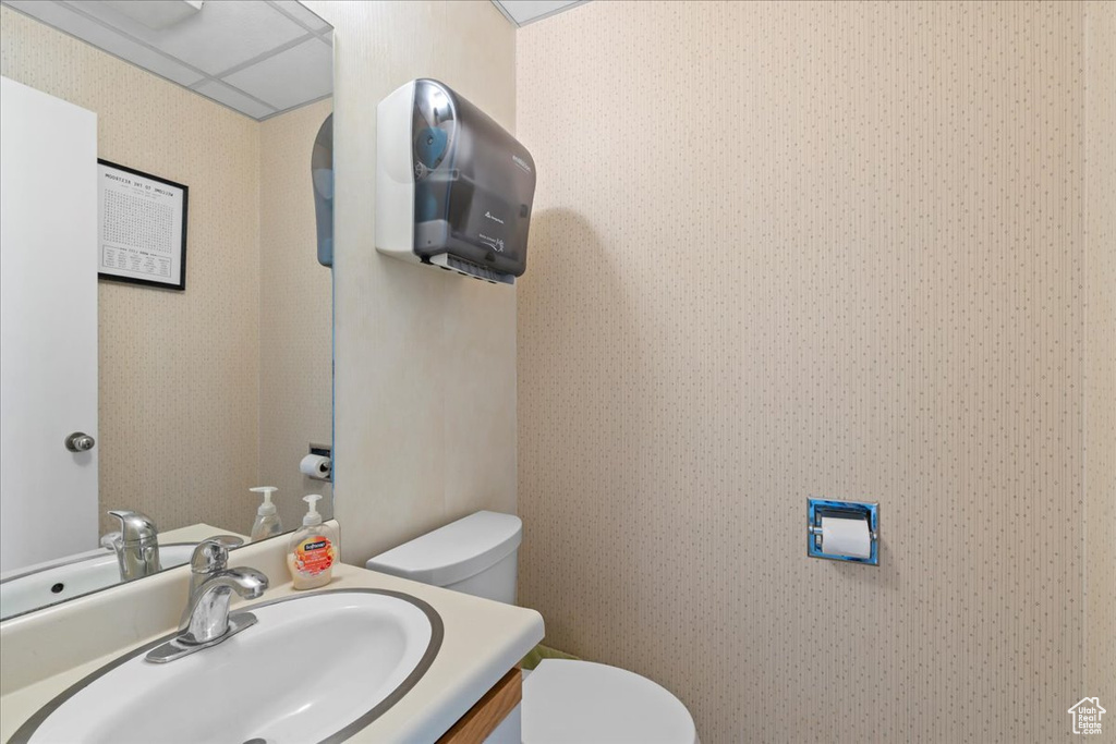 Half bath featuring toilet, wallpapered walls, and vanity