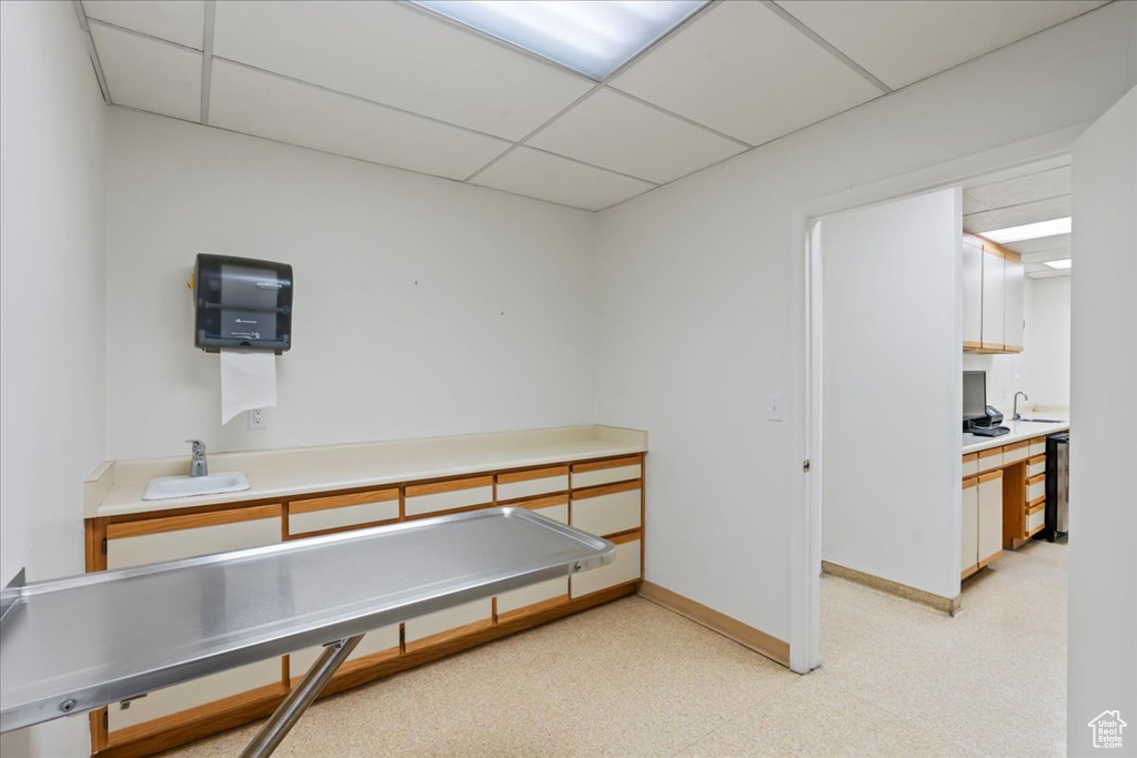 Rec room featuring a drop ceiling, baseboards, a sink, and light flooring