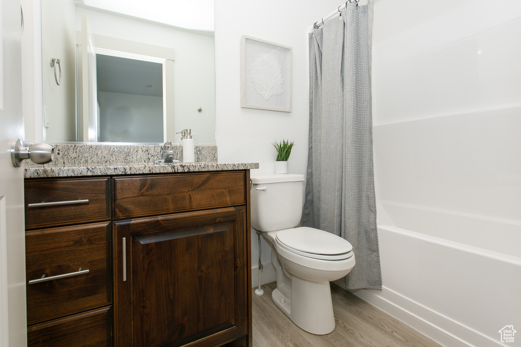 Full bath featuring wood finished floors, toilet, vanity, and shower / bath combo