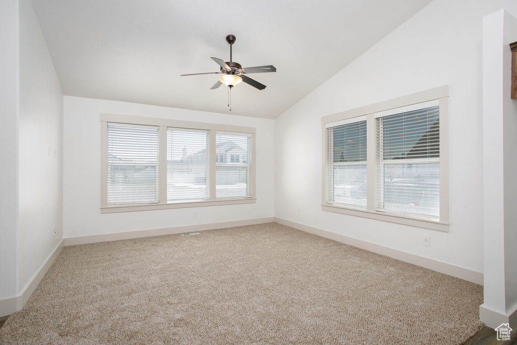 Spare room with vaulted ceiling, carpet floors, a ceiling fan, and baseboards