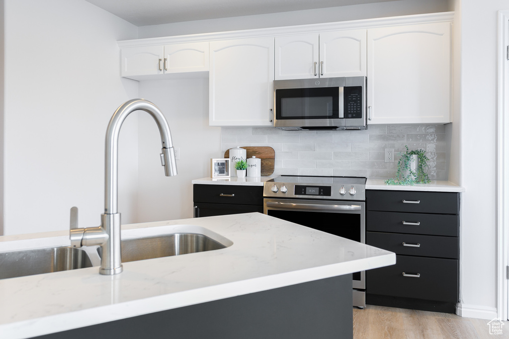 Kitchen with appliances with stainless steel finishes, white cabinetry, a sink, tasteful backsplash, and light wood finished floors