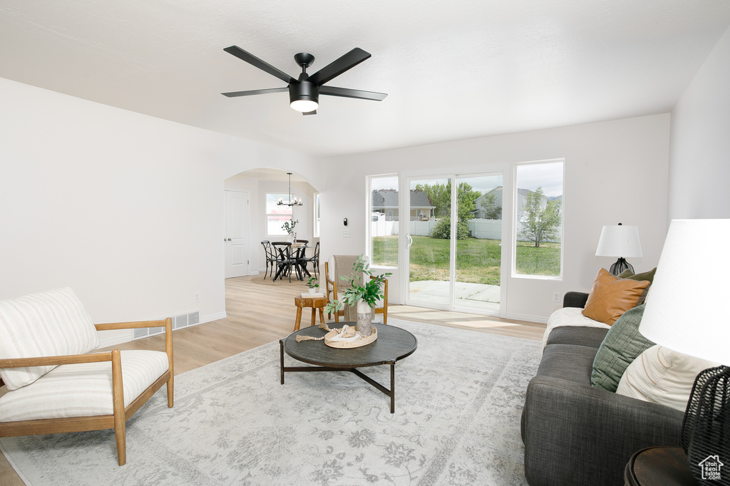 Living room featuring arched walkways, a chandelier, light wood-type flooring, a ceiling fan, and baseboards