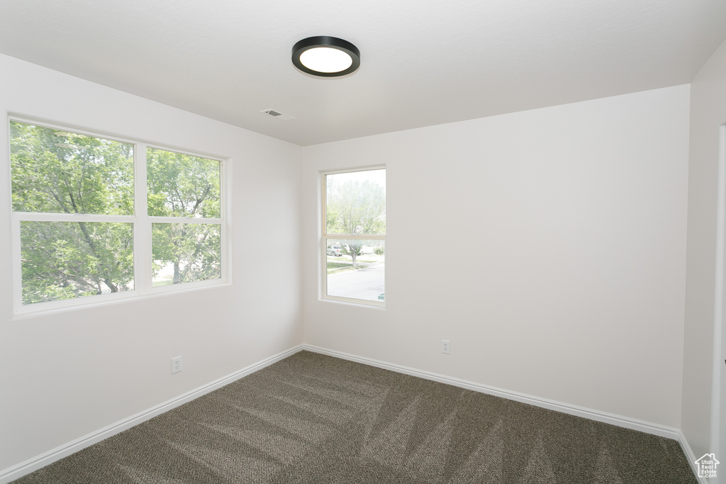 Empty room with dark colored carpet, plenty of natural light, and baseboards