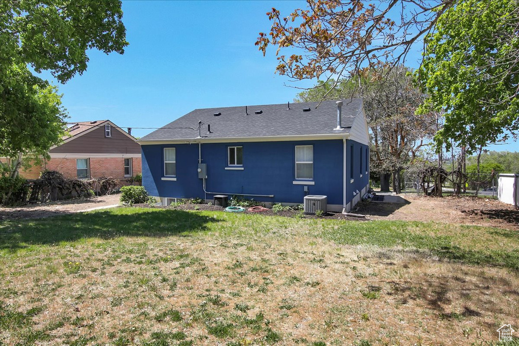 Rear view of house with roof with shingles, central AC, and a lawn