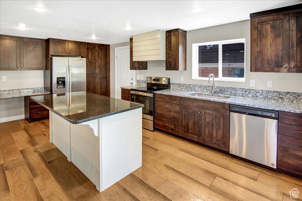Kitchen with appliances with stainless steel finishes, a sink, light wood-style floors, recessed lighting, and light stone countertops