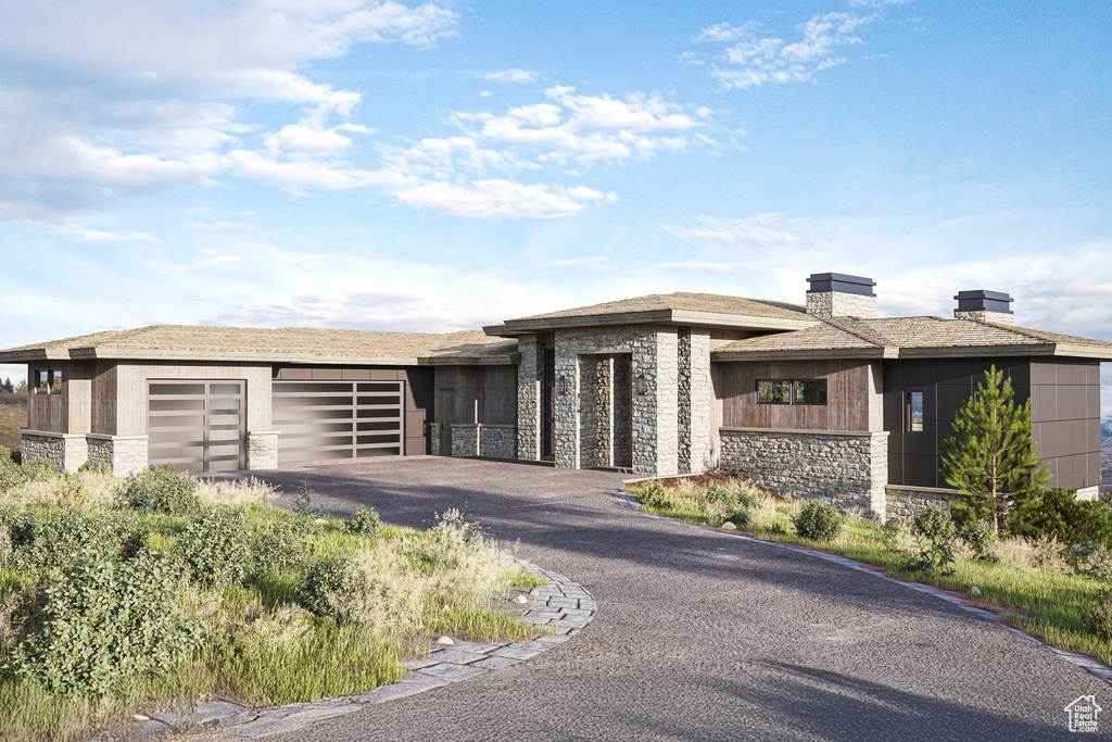 Prairie-style home with stone siding, an attached garage, and driveway