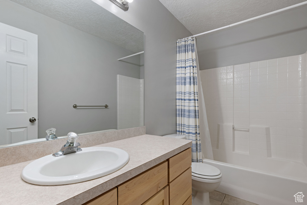 Full bathroom with a textured ceiling, toilet, vanity, shower / tub combo, and tile patterned floors