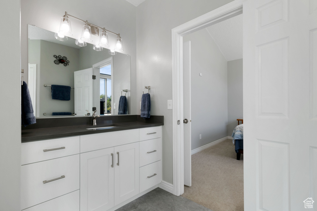Ensuite bathroom with vanity, baseboards, and vaulted ceiling