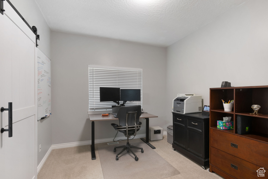 Home office featuring a barn door, light carpet, baseboards, and a textured ceiling