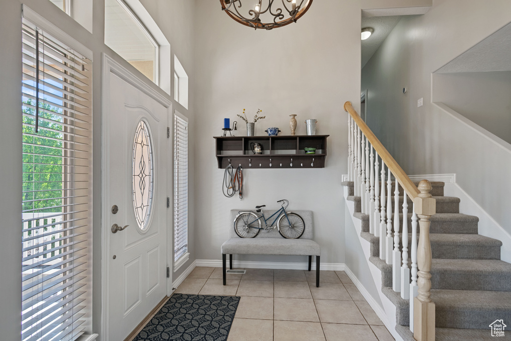 Entryway with light tile patterned floors, stairway, a chandelier, baseboards, and a high ceiling