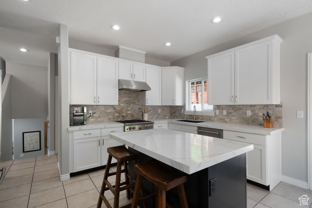 Kitchen featuring under cabinet range hood, a sink, light tile patterned floors, tasteful backsplash, and recessed lighting