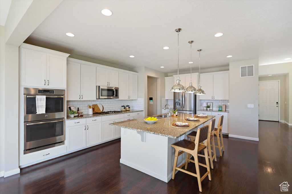 Kitchen featuring appliances with stainless steel finishes, a sink, decorative backsplash, a kitchen island with sink, and dark wood-style floors