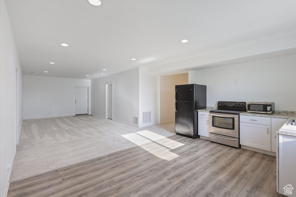 Kitchen featuring appliances with stainless steel finishes, white cabinetry, light stone countertops, light wood-type flooring, and recessed lighting