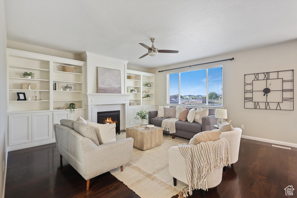 Living area featuring a ceiling fan, a tiled fireplace, baseboards, and dark wood-type flooring