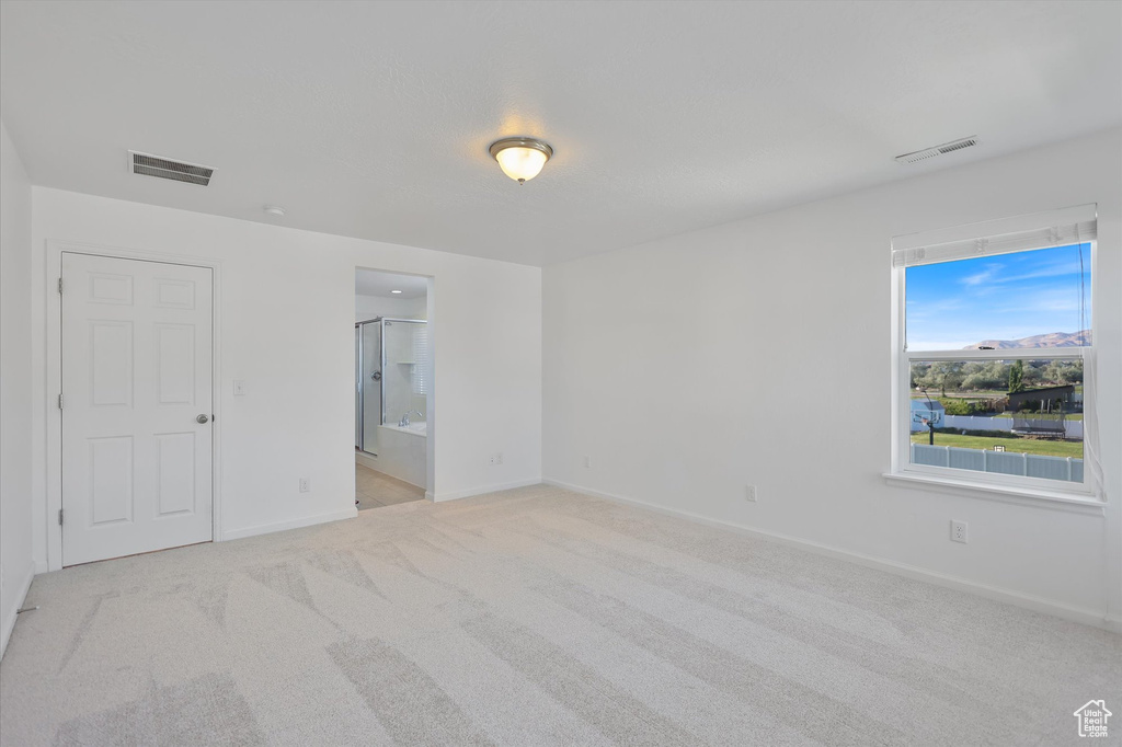 Unfurnished bedroom with light carpet, baseboards, and ensuite bath