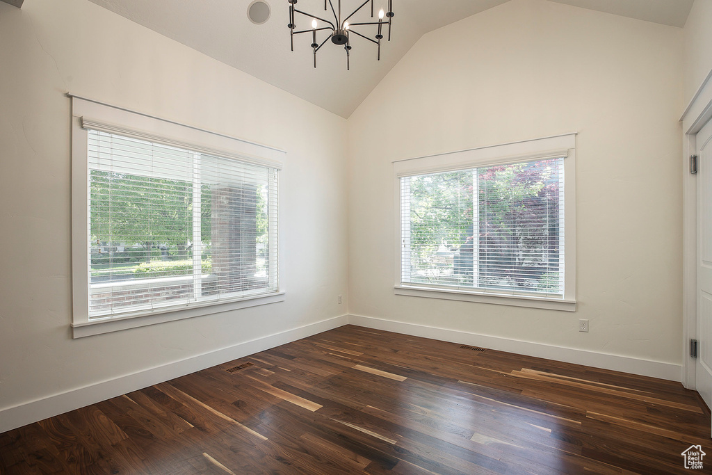 Unfurnished room featuring dark wood-style flooring, a chandelier, baseboards, and high vaulted ceiling