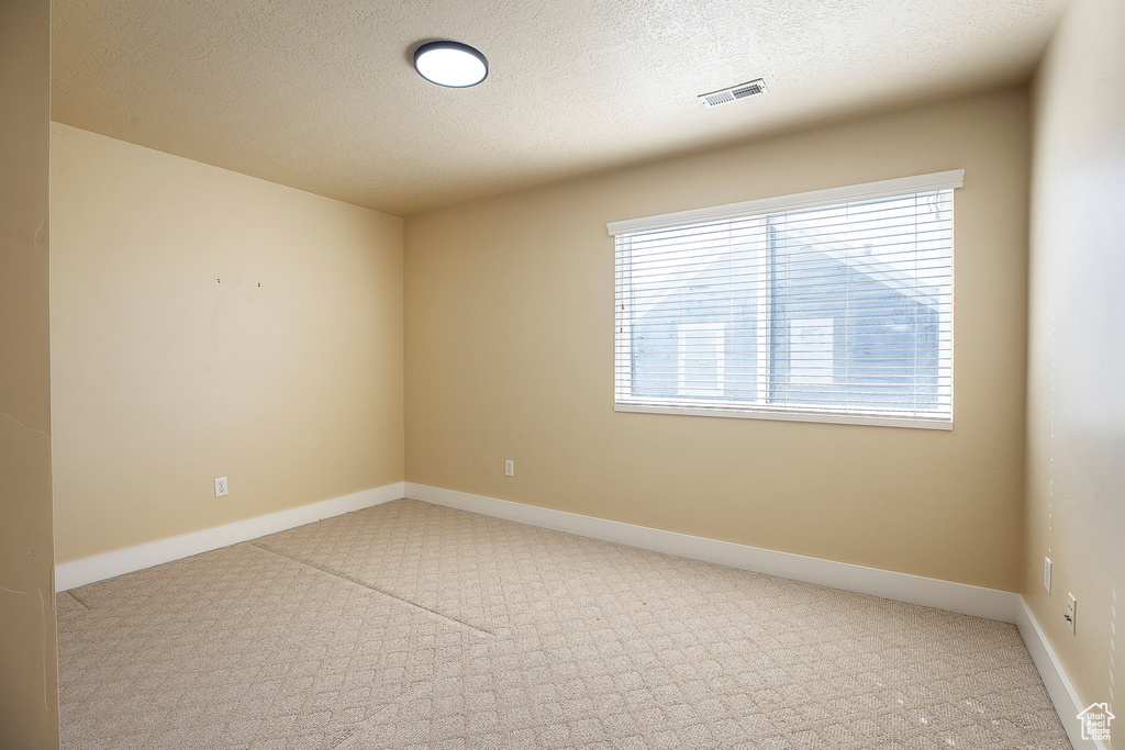 Empty room with carpet flooring, a textured ceiling, and baseboards