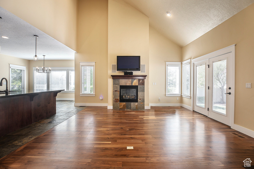 Living area with a textured ceiling, a tiled fireplace, a chandelier, high vaulted ceiling, and baseboards