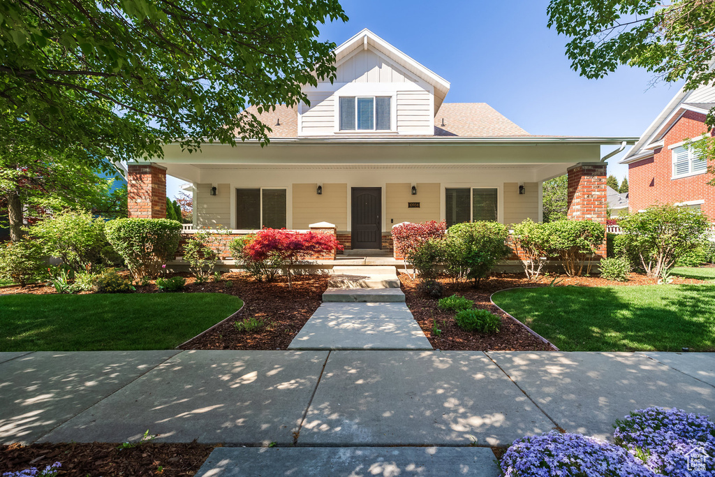 View of front facade featuring covered porch, a front lawn, and board and batten siding
