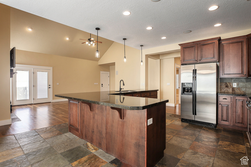 Kitchen featuring stainless steel fridge with ice dispenser, dark countertops, a sink, stone tile flooring, and a textured ceiling