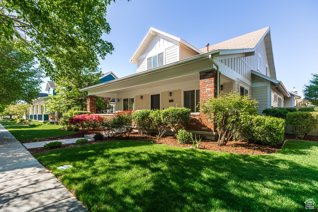 View of front facade with brick siding, a front yard, a porch, and board and batten siding