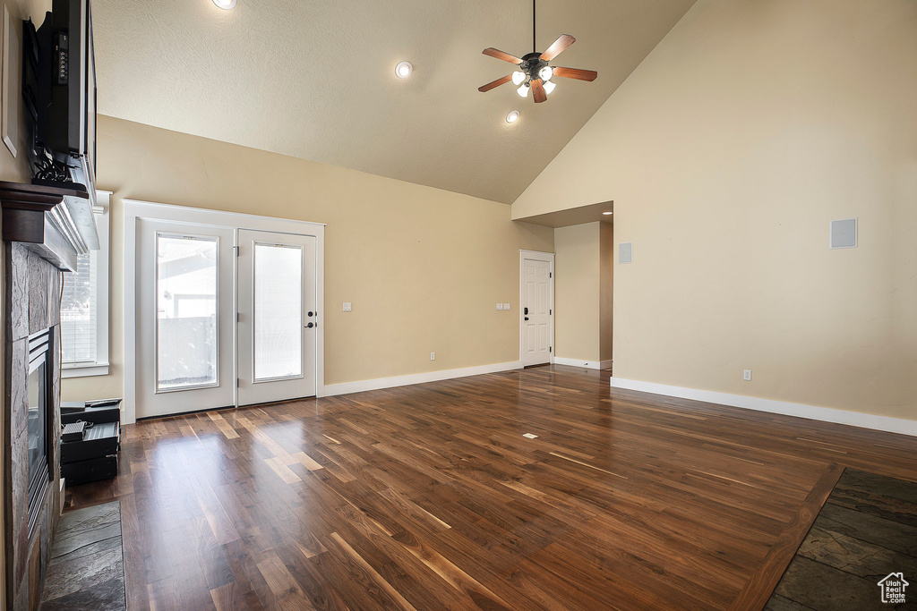 Unfurnished living room featuring ceiling fan, dark wood-style floors, high vaulted ceiling, a fireplace, and baseboards
