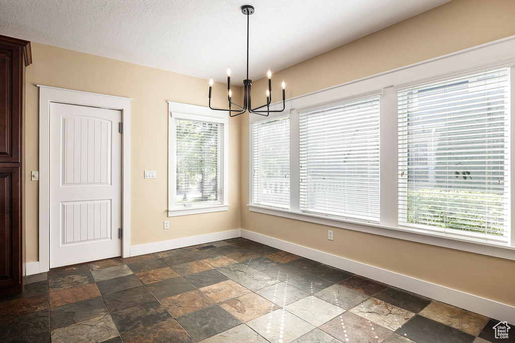 Unfurnished dining area with stone tile flooring, baseboards, and a chandelier