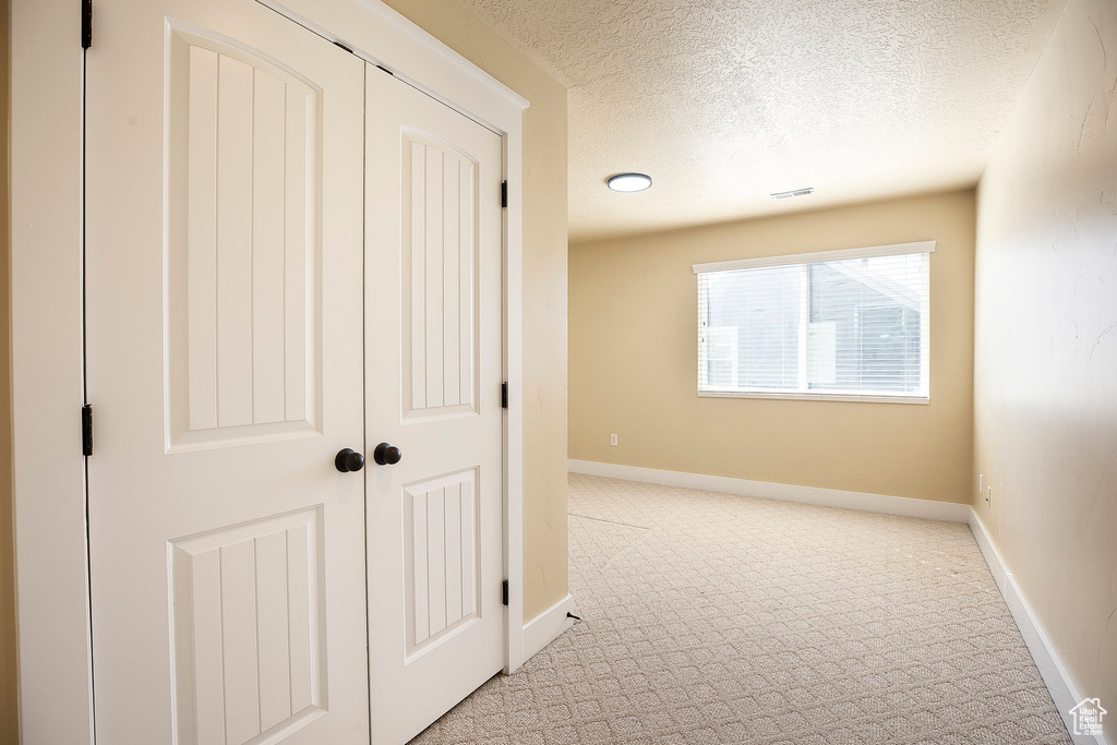 Hallway with light carpet, a textured ceiling, and baseboards