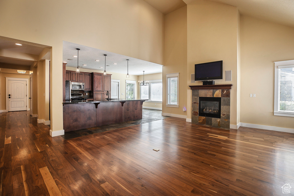 Kitchen featuring a breakfast bar area, high vaulted ceiling, open floor plan, dark wood-style flooring, and stainless steel microwave