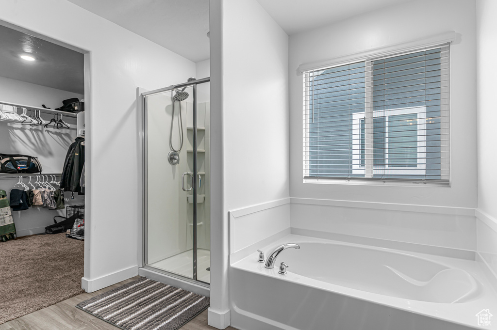 Full bathroom featuring a stall shower, a spacious closet, wood finished floors, and a garden tub
