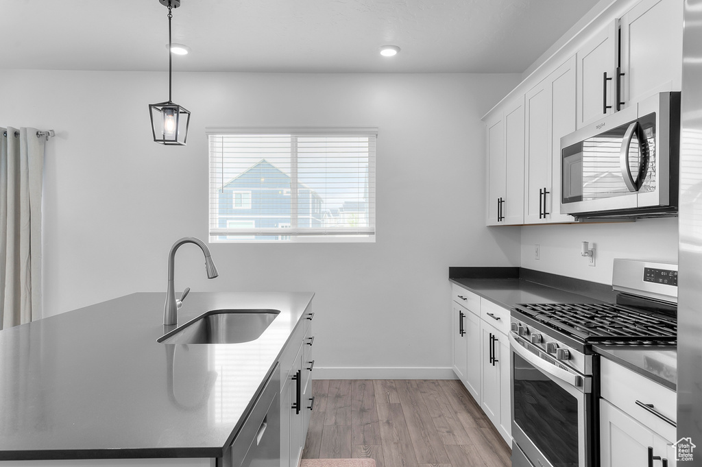 Kitchen with appliances with stainless steel finishes, a sink, light wood-style floors, dark countertops, and white cabinetry