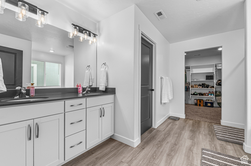 Full bathroom with wood finished floors, double vanity, a walk in closet, and baseboards