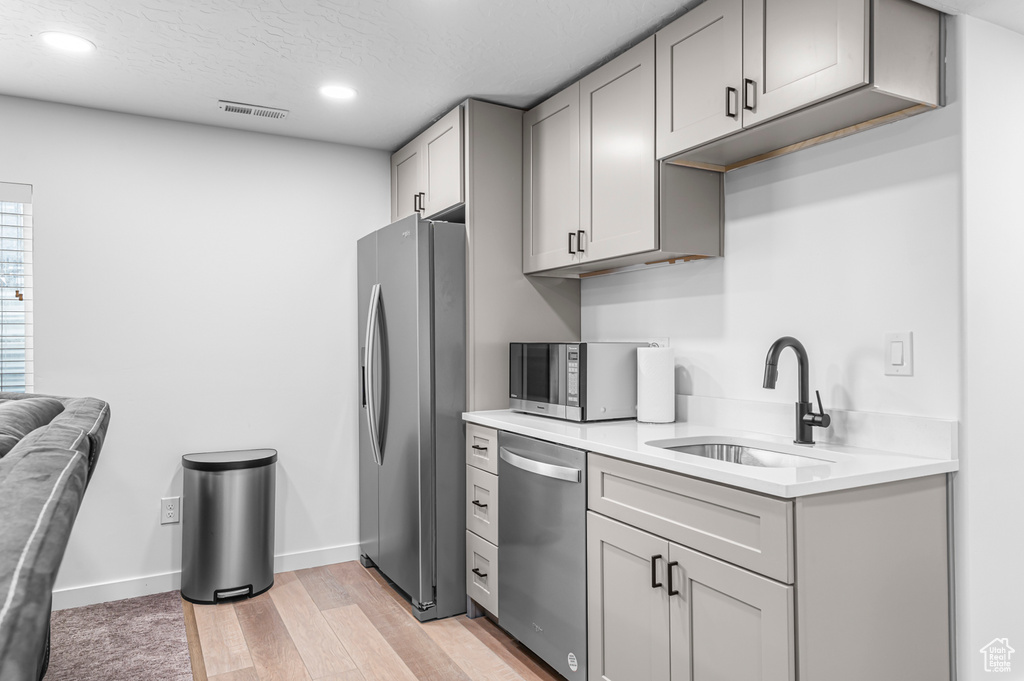 Kitchen with appliances with stainless steel finishes, a sink, gray cabinetry, light countertops, and recessed lighting