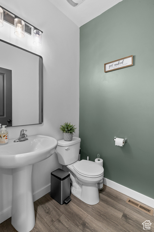 Half bath with baseboards, toilet, wood finished floors, and a sink