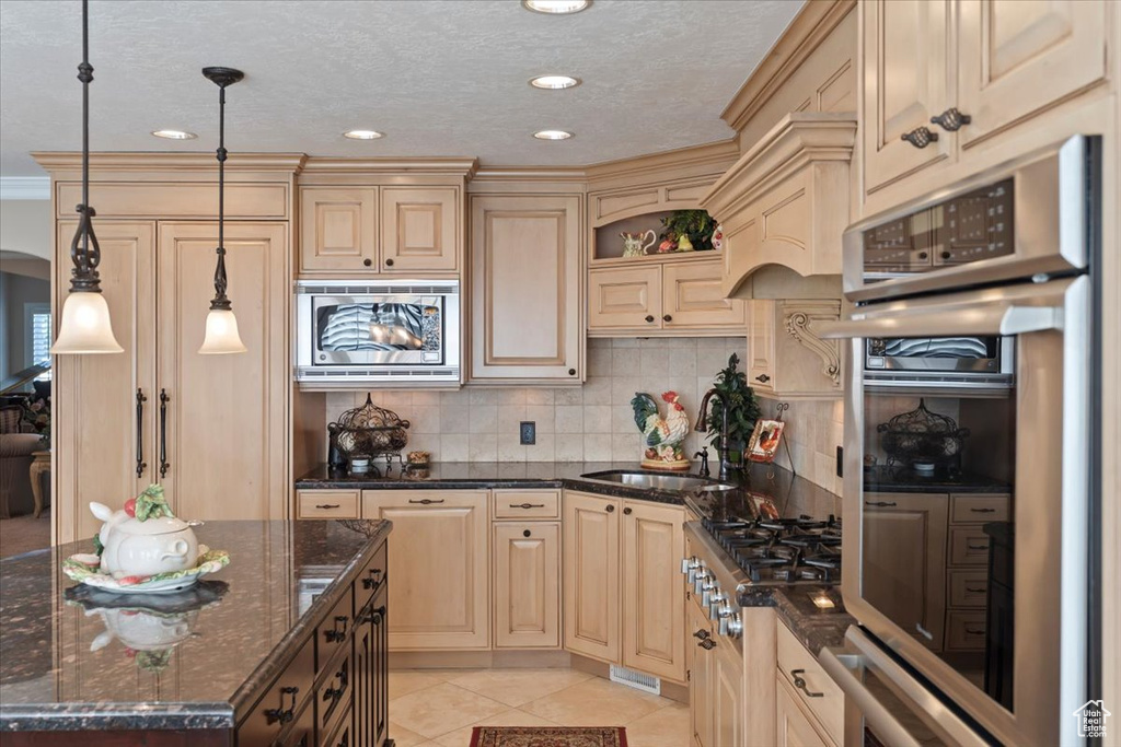 Kitchen featuring stainless steel appliances, a sink, tasteful backsplash, light tile patterned flooring, and cream cabinetry