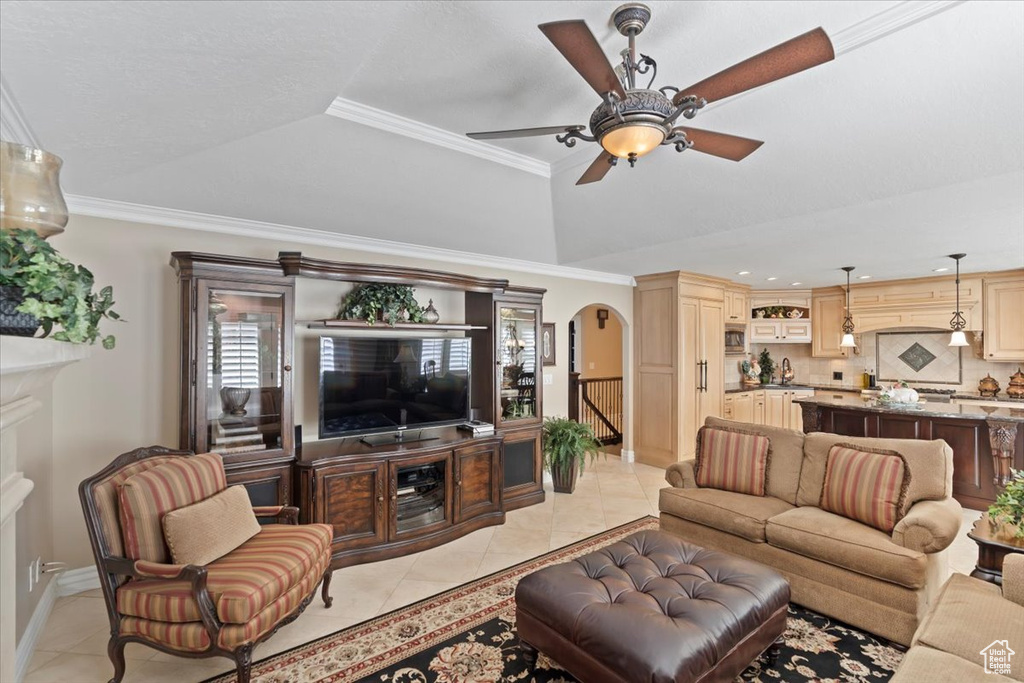 Living room with arched walkways, light tile patterned floors, a raised ceiling, a ceiling fan, and crown molding