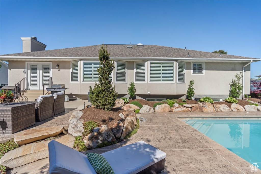Rear view of house with a patio, french doors, stucco siding, an outdoor pool, and a chimney