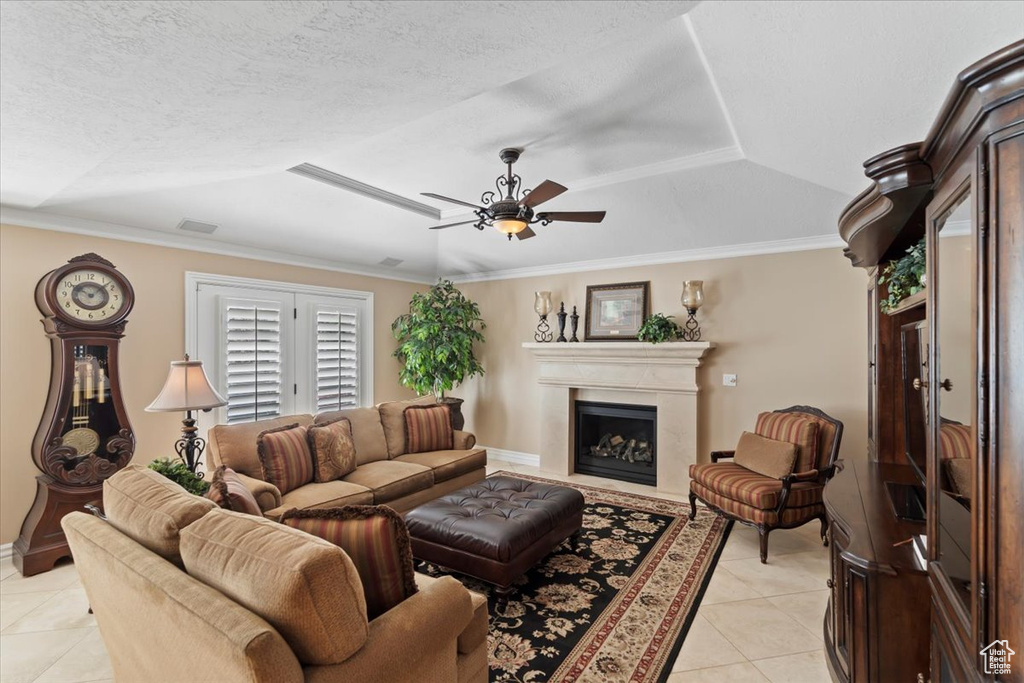 Living area with light tile patterned floors, a ceiling fan, a tray ceiling, a fireplace, and crown molding