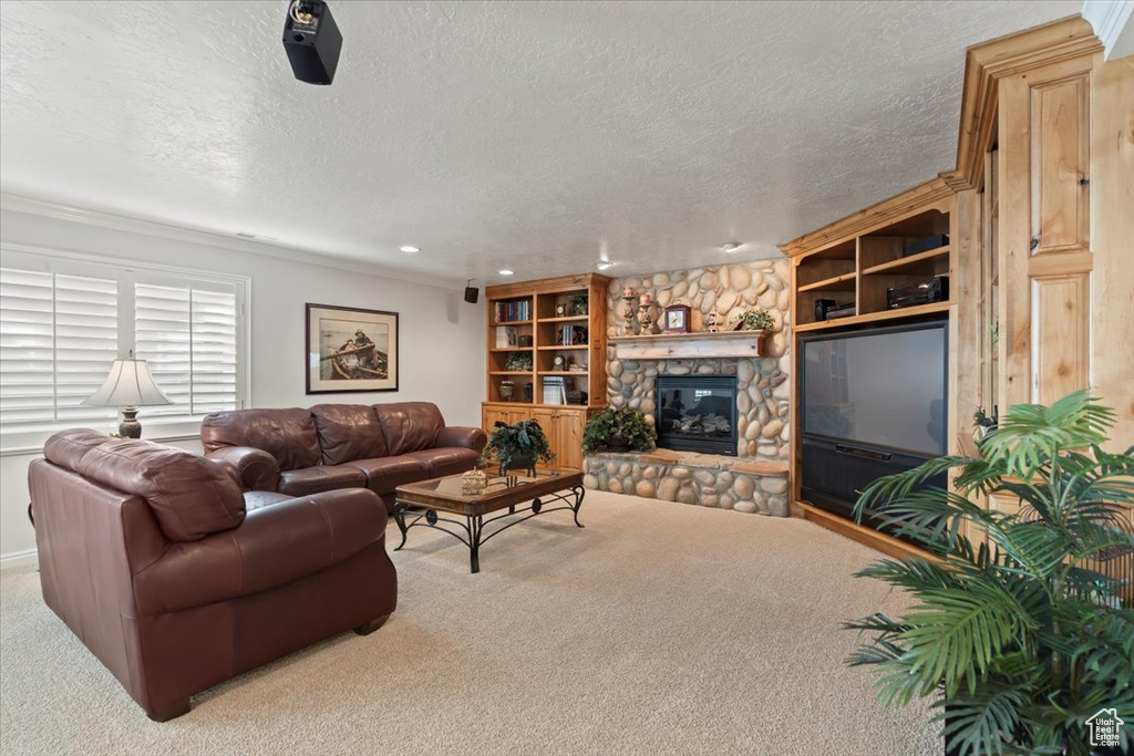 Living room with carpet, a textured ceiling, a stone fireplace, crown molding, and recessed lighting