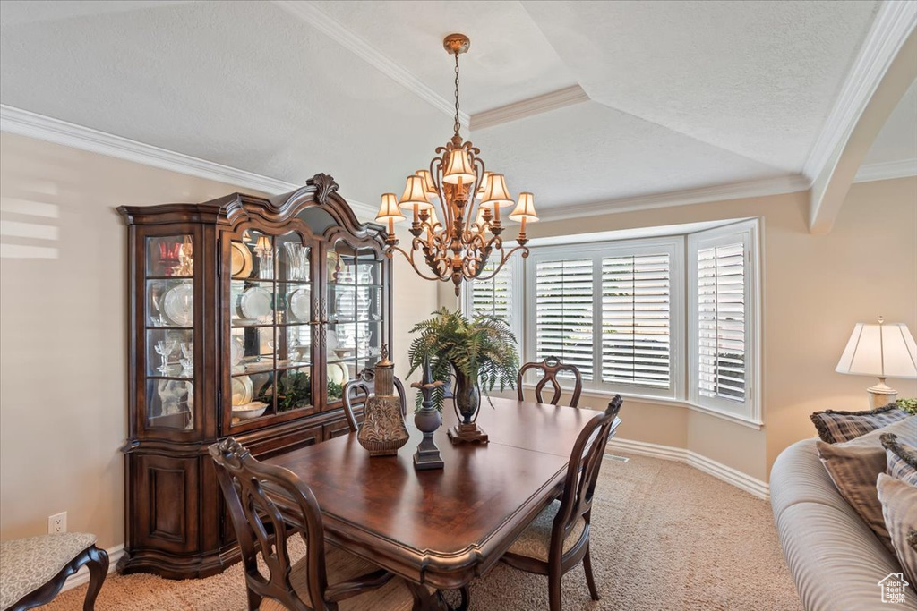 Dining area with a chandelier, light colored carpet, ornamental molding, and baseboards
