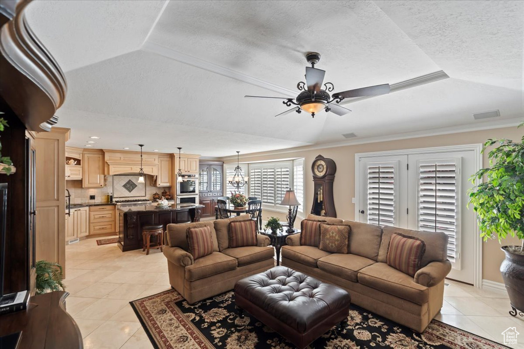 Living area featuring light tile patterned flooring, a ceiling fan, a textured ceiling, a raised ceiling, and crown molding