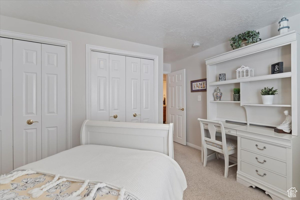 Bedroom featuring light carpet, multiple closets, baseboards, and a textured ceiling