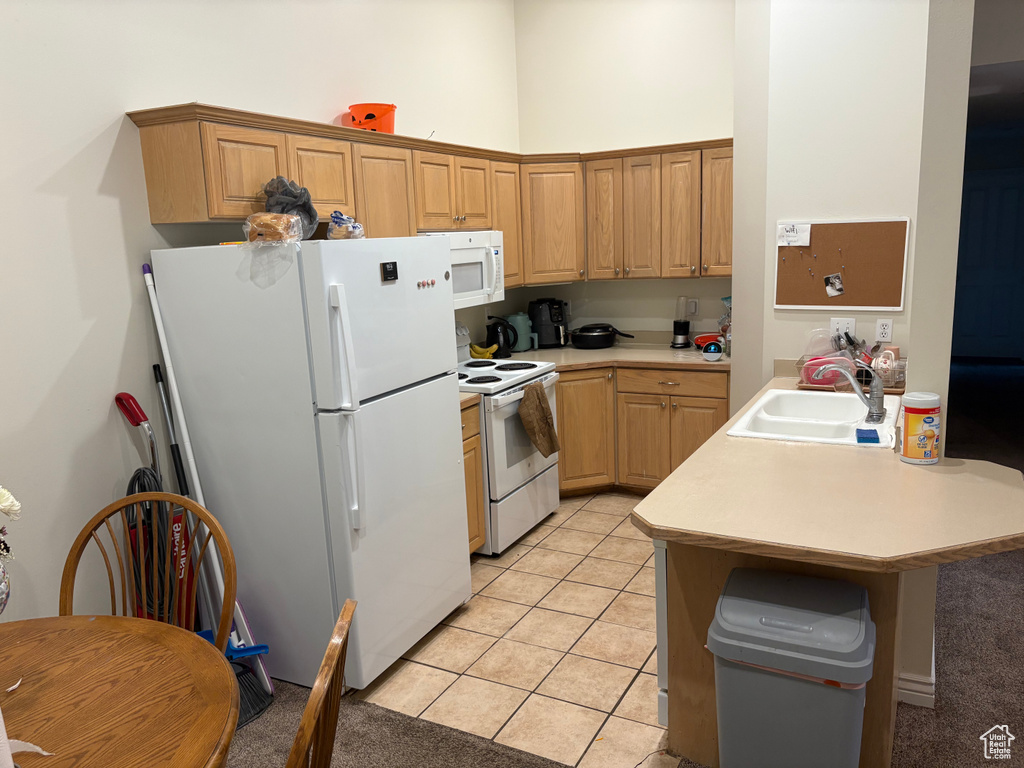 Kitchen with white appliances, a sink, light countertops, light tile patterned floors, and a peninsula