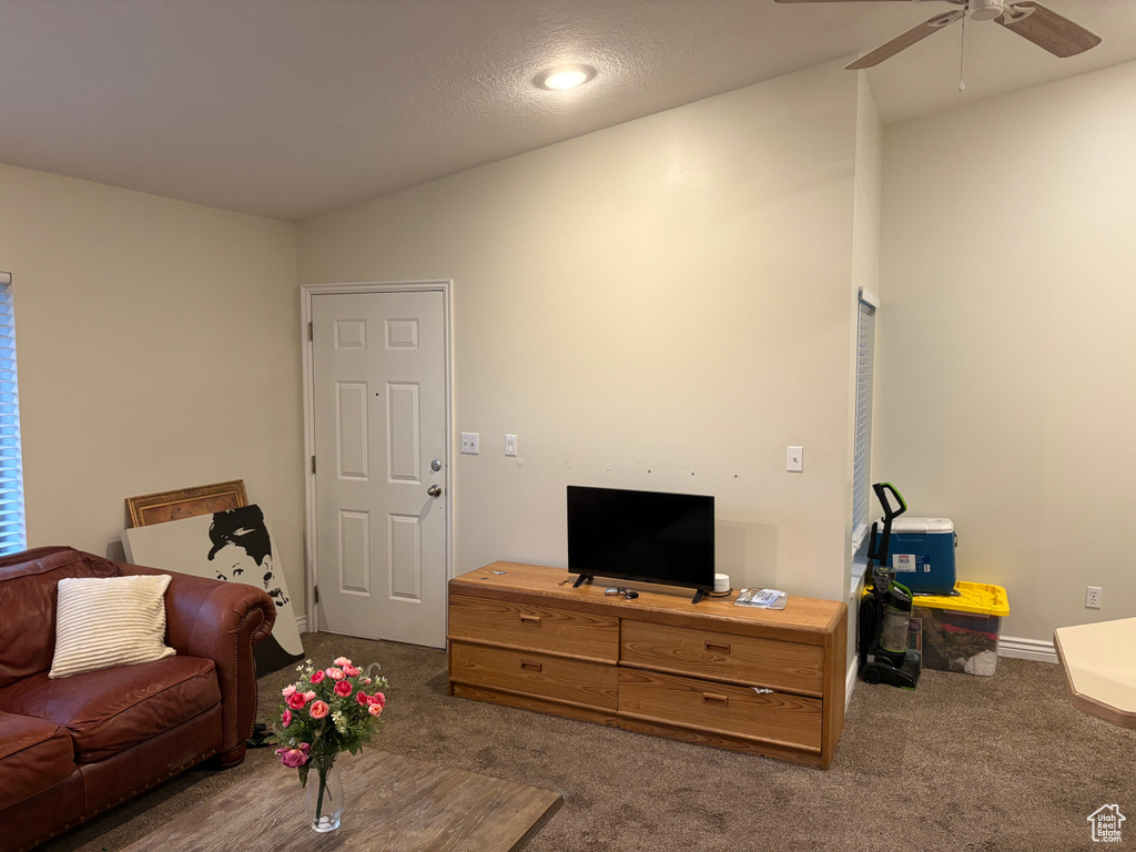Carpeted living area featuring a ceiling fan and baseboards